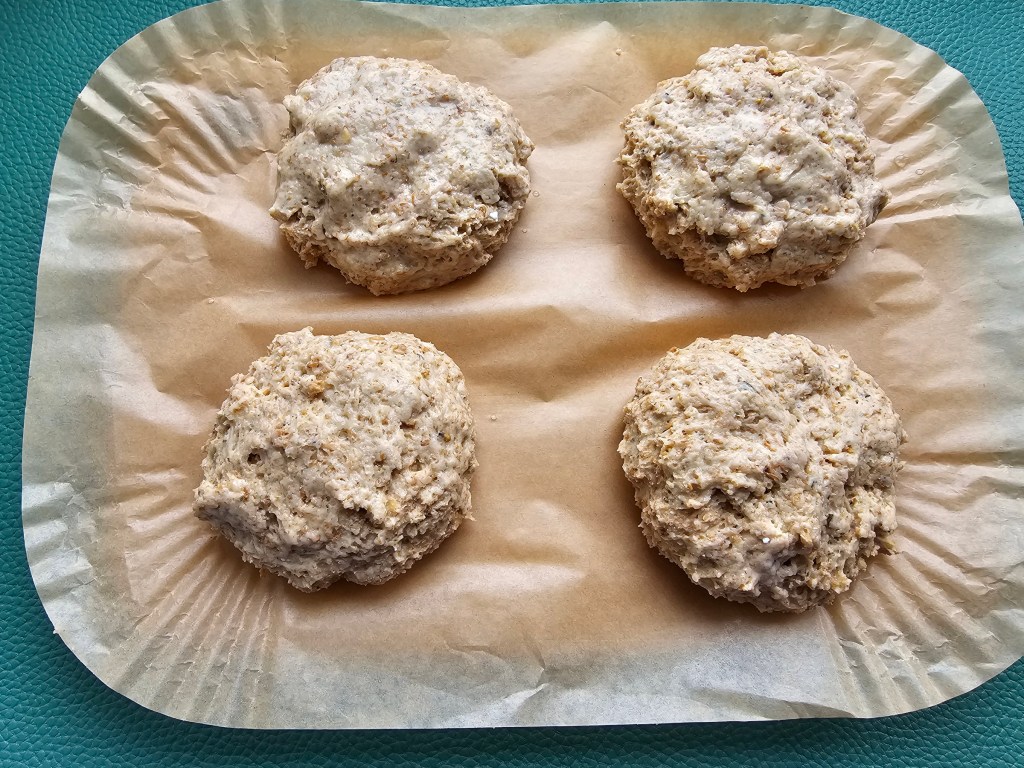Four dough balls on a sheet of baking paper, for making protein cottage cheese bread rolls.