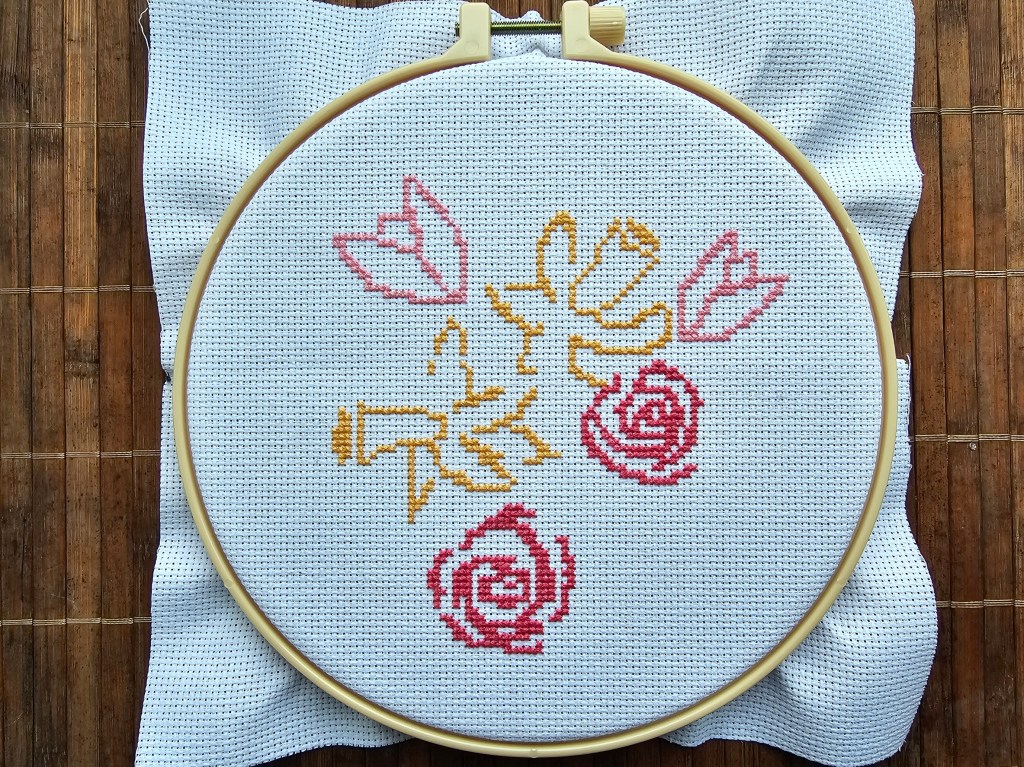 Half finished cross stitch design featuring daffodils, roses and tulips. The outline of daffodils, tulips and roses is done.