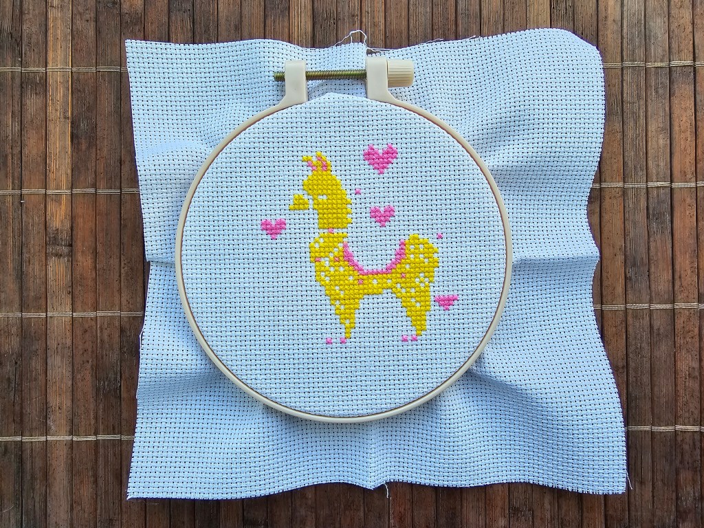 Half finished cross stitch design featuring a golden llama with pink hearts.