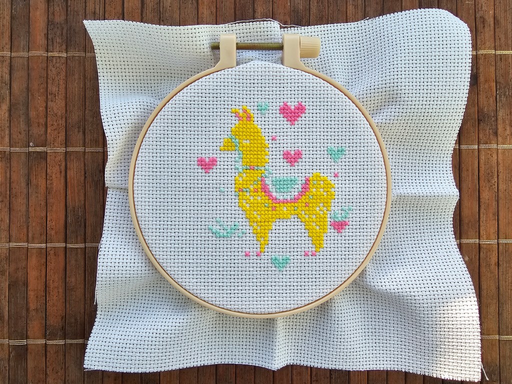 Half finished cross stitch design featuring a golden llama with pink and teal hearts.
