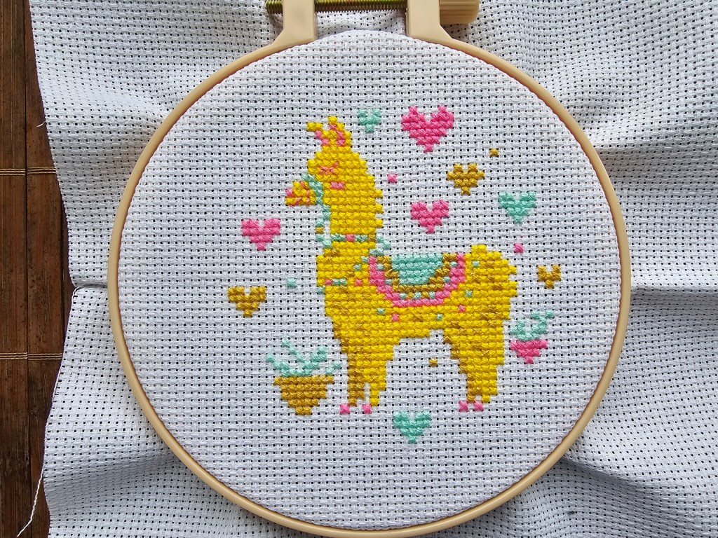 Completed cross stitch design featuring a golden llama and pink and teal hearts.