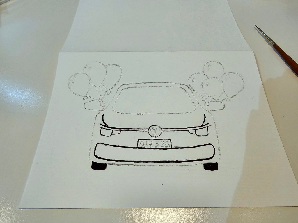 A silver Volkswagen car with balloons attached to mirrors. A DIY birthday card painted with acrylics. Most of the car is still a sketch.