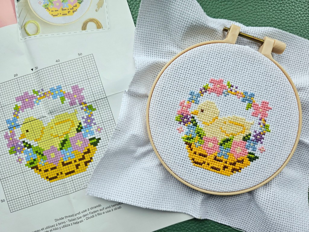 Finished cross stitch design featuring a chick inside a basket decorated with flowers.