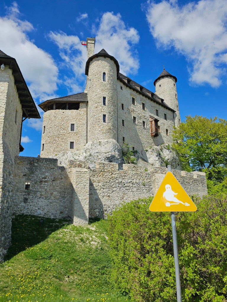 Bobolice Castle in Poland. There's a yellow sign with a ghost in front of the castle, indicating that the castle is haunted.