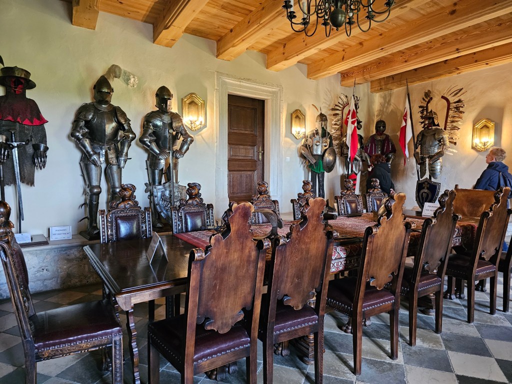 A room with a long, wooden table and medieval armour in Bobolice Castle.