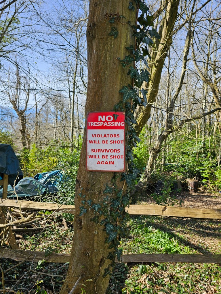 A funny sign bewaring trespassers, hanging on a tree.