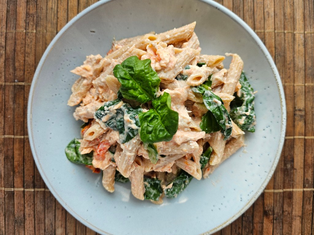Salmon and tomato pasta, served on a plate, garnished with spinach.