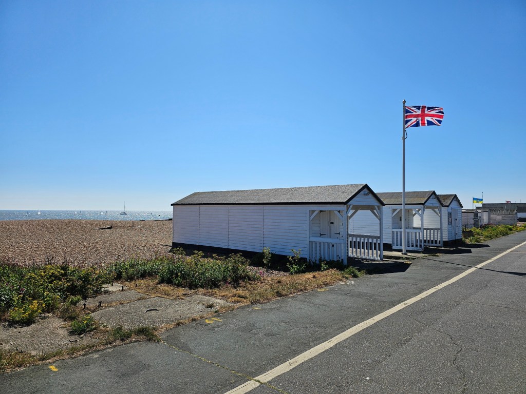 Small, white beach houses and a British flag waving in the wind. English Channel can be seen in the background.