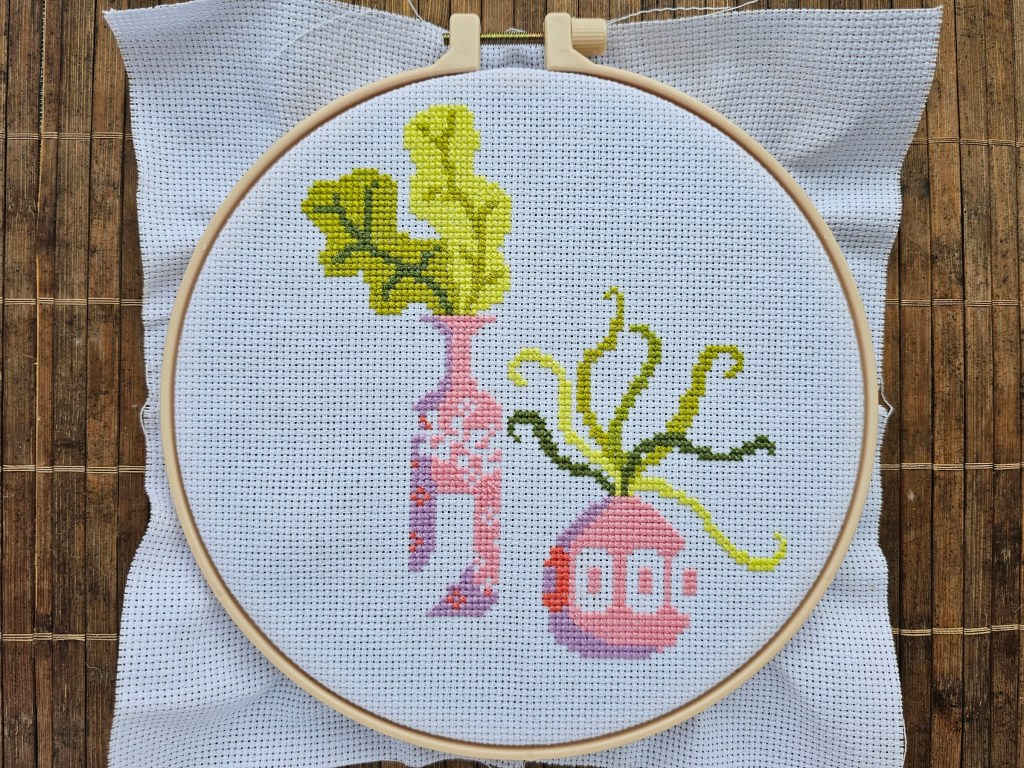 Two pink and purple vases cross stitched onto a blank aida.