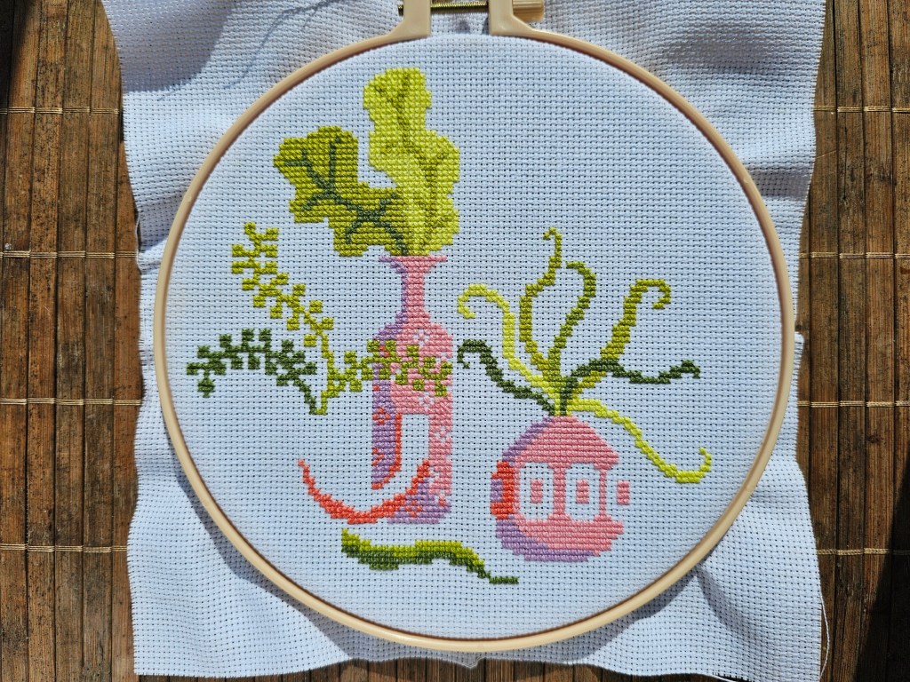 Three cross stitch vases filled with green plants.