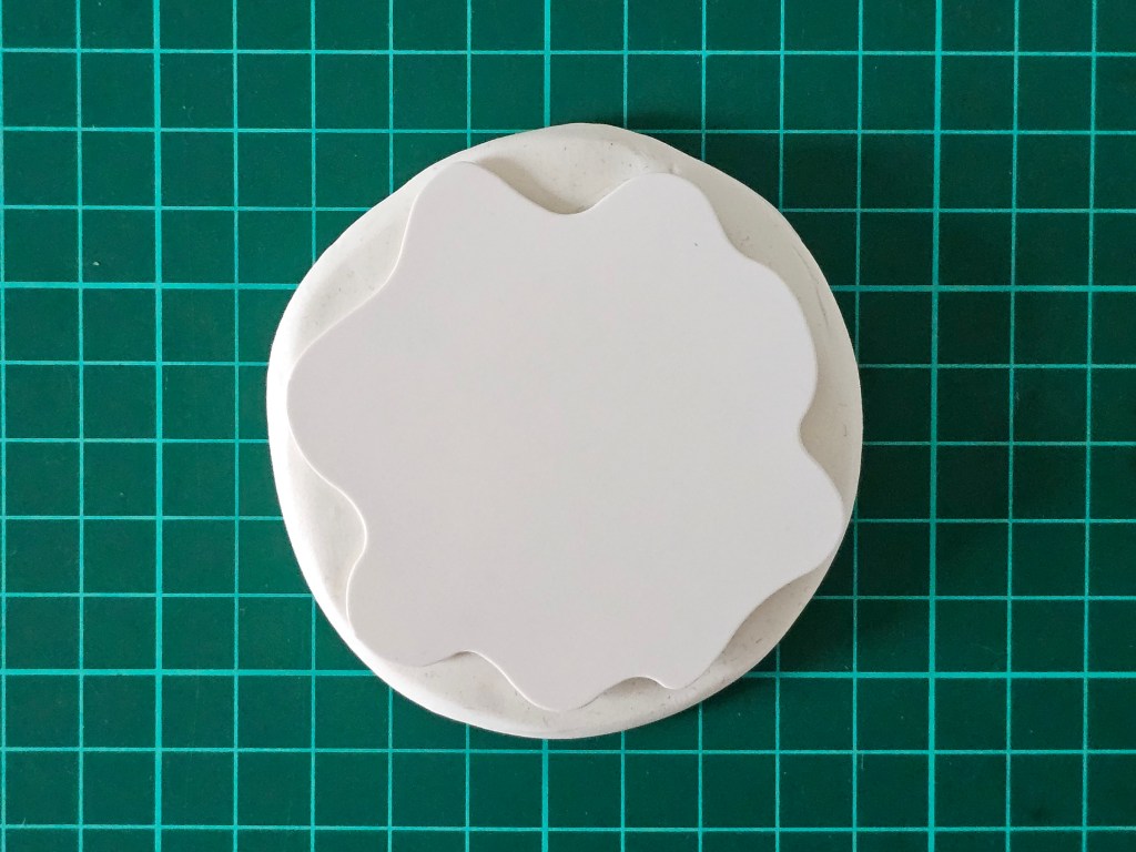 Abstract stencil placed on top of a rolled out circle of white polymer clay.