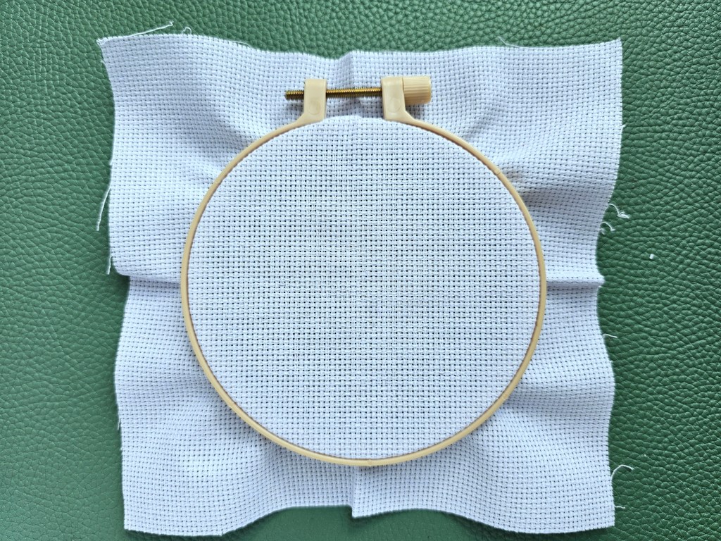 Plastic embroidery hoop with a blank aida mounted.