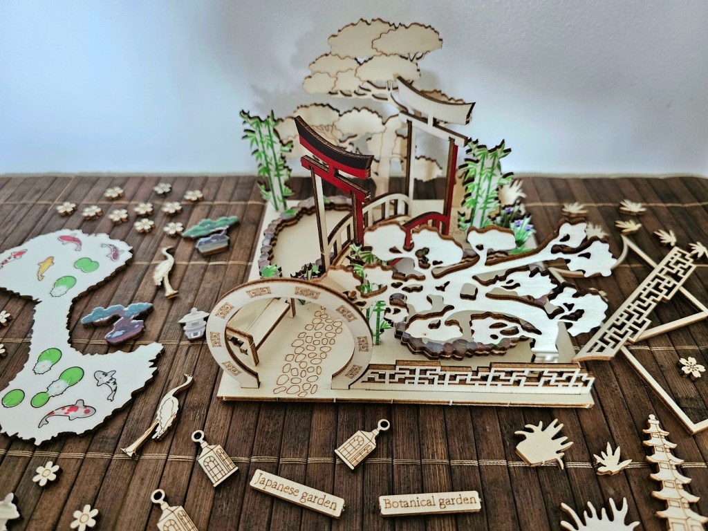 Roughly assembled scene for a wooden Japanese garden. Unpainted elements are arranged on the base sheet. Smaller pieces are scattered around the table.