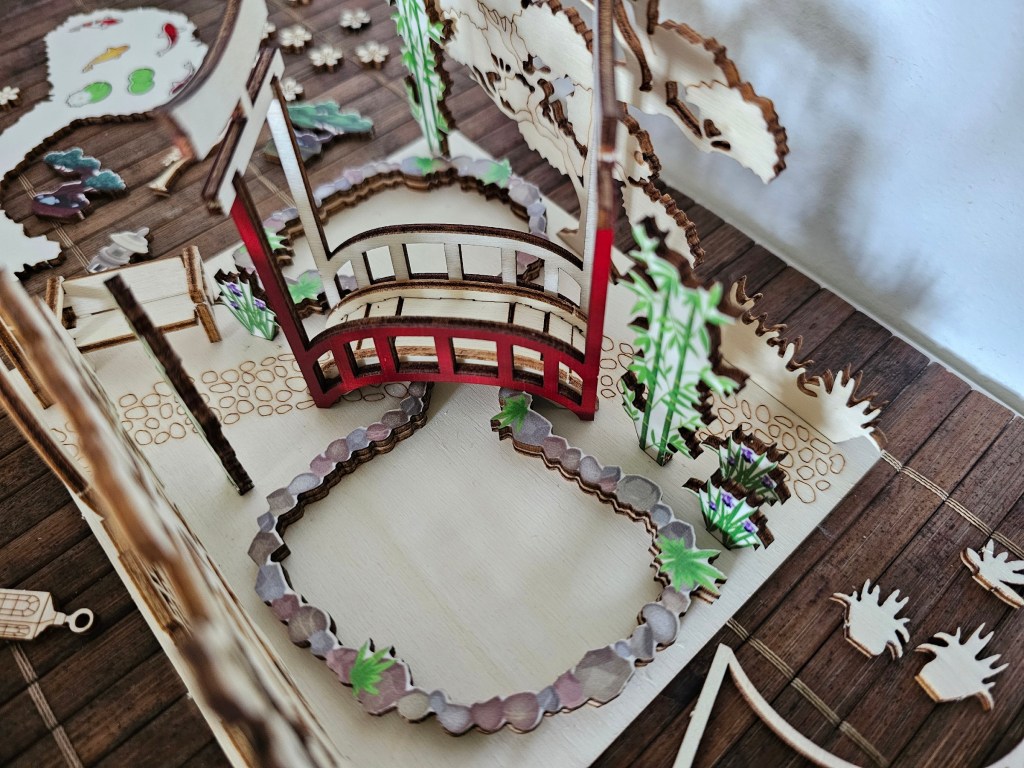 Roughly assembled scene for a wooden Japanese garden. Unpainted elements are arranged on the base sheet. Smaller pieces are scattered around the table.