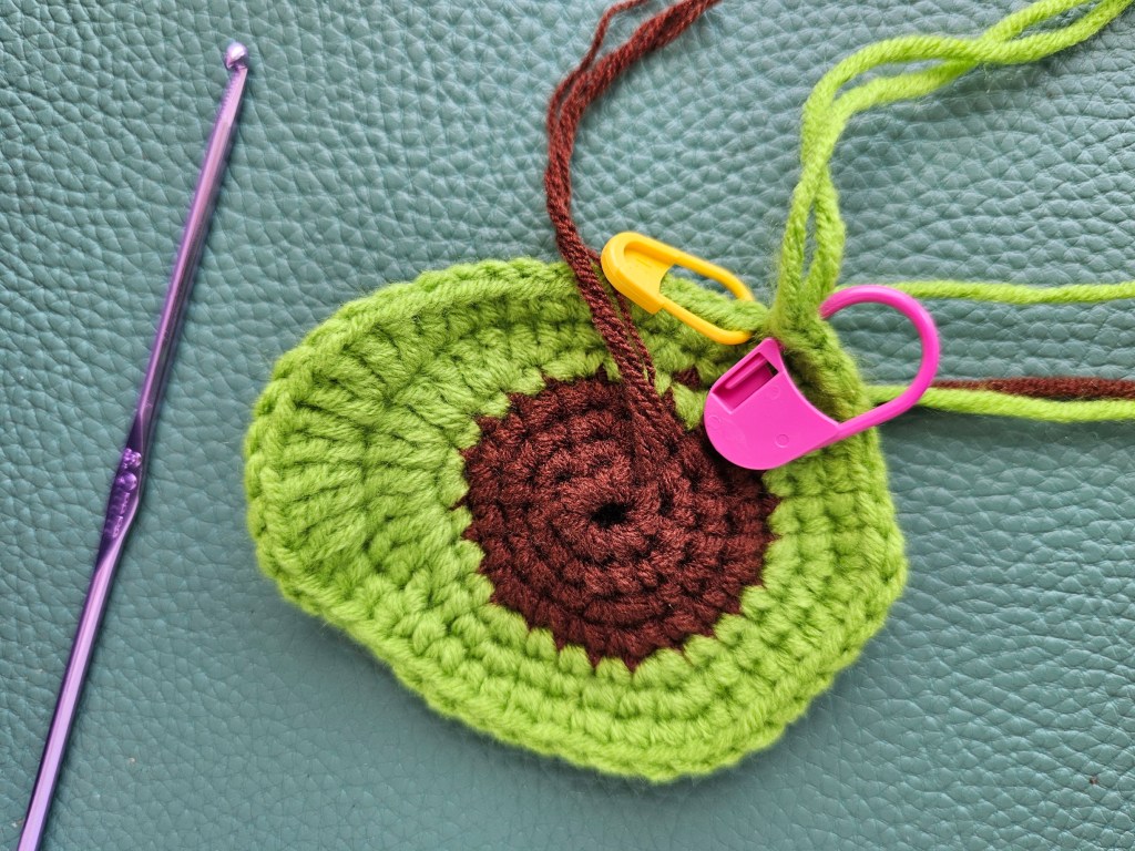 A crocheted circle made with brown yarn in the middle and green on the outside.