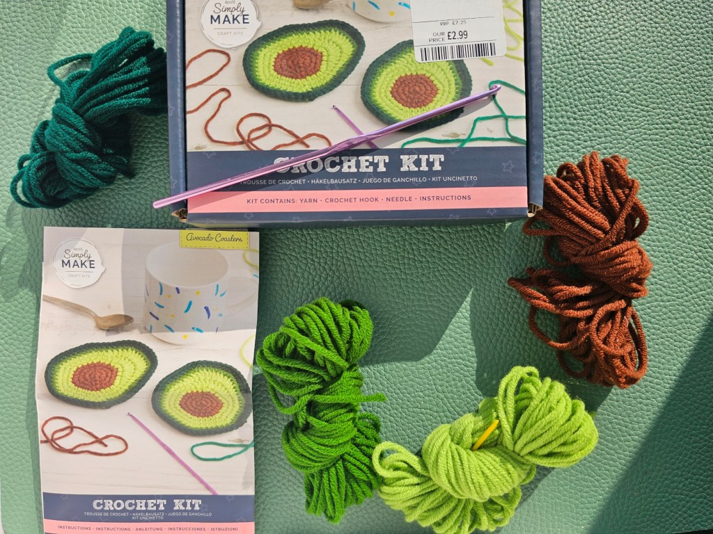 Contents of a DIY crochet kit for making avocado coasters. It includes a crochet hook and yarn in four colours.