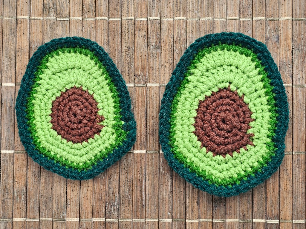 Two finished handmade crocheted coasters resembling sliced avocado.