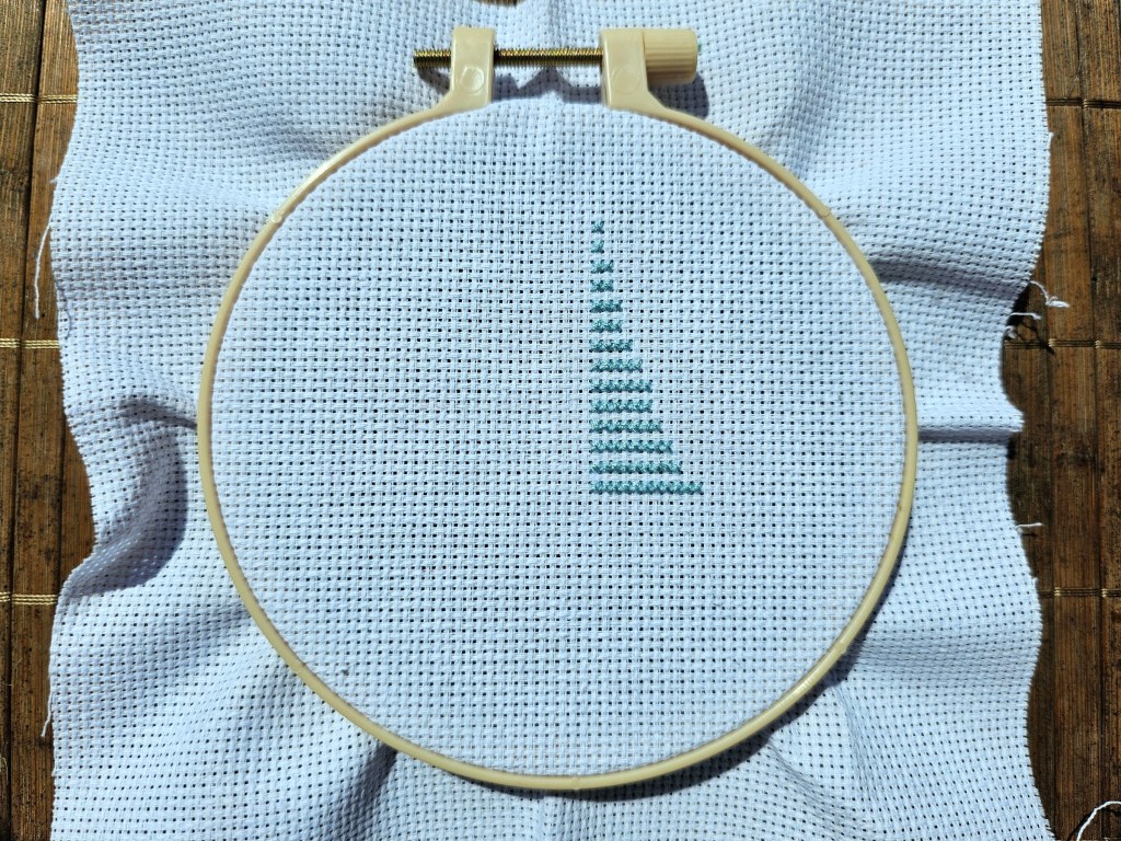 The first few rows of stitches for a small cross stitch sailboat design.