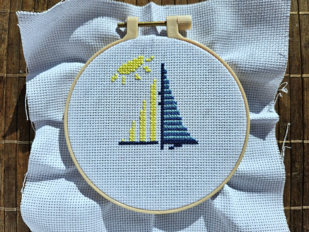 Partially completed cross stitch project with a small sailboat design.