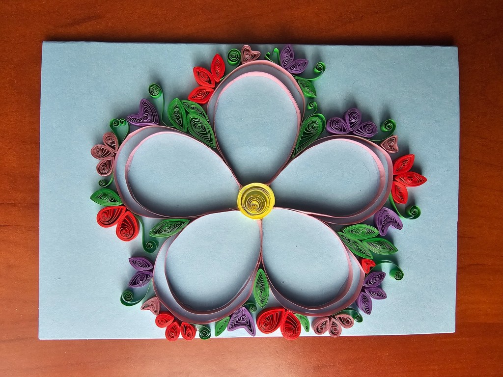A simple handmade quilled card. It features a large, hollow flower framed with smaller flowers and leaves.