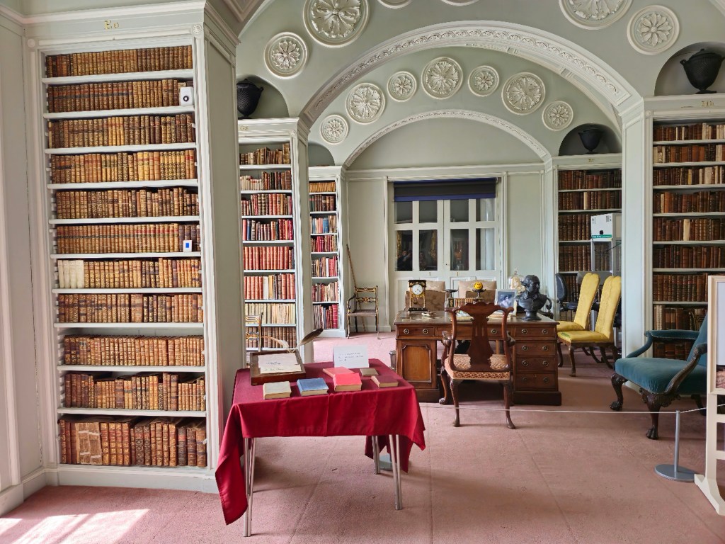 A bright room with loads of bookcases with old books and comfortable chairs in Wimpole Hall.