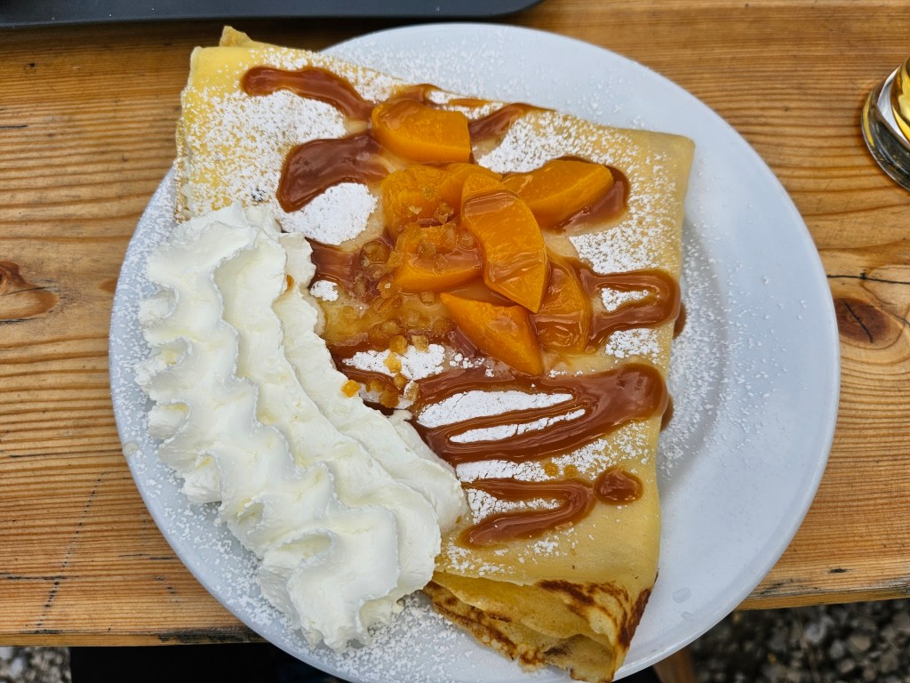 A large crepe with fruit and whipped cream, on a plate.