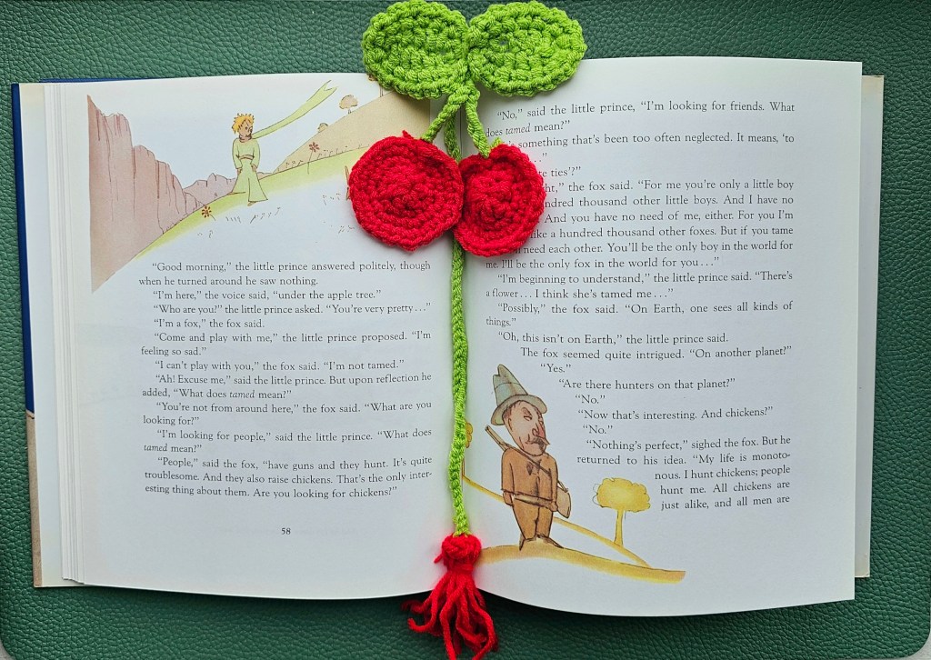 A bookmark with crocheted red cherries, placed on an open book