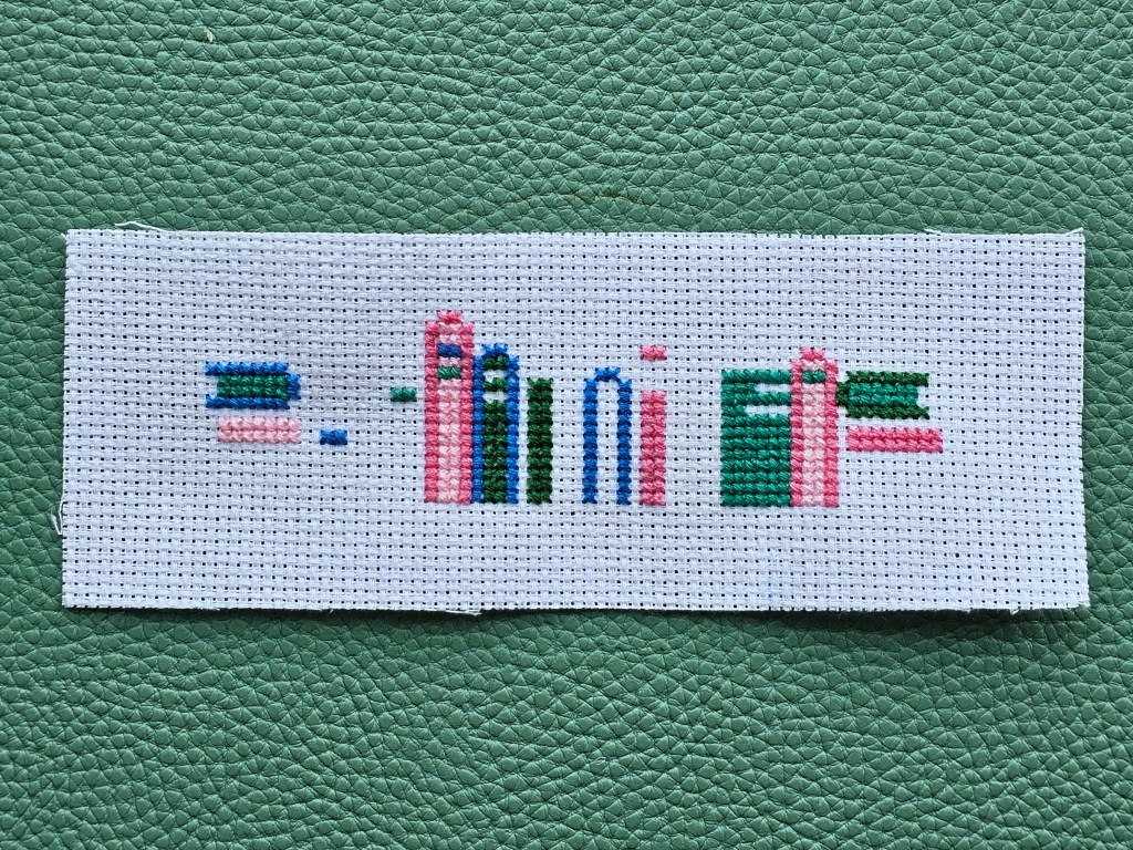 Partially completed cross stitch bookmark. Blue, green and pink elements are done.