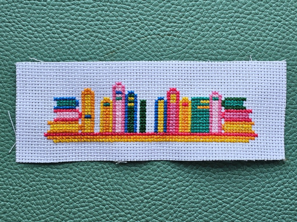 Nearly completed cross stitch bookmark with a design featuring a shelf with colourful books.