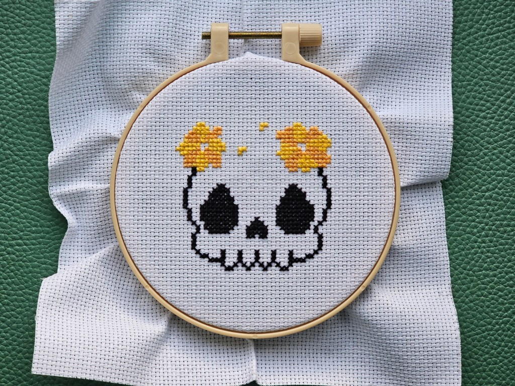 A black outline of a cross stitched skull with two yellow flowers