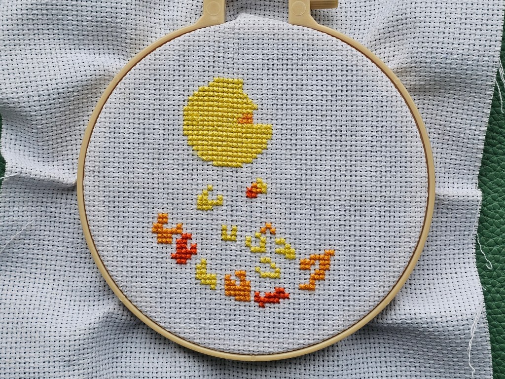 The process of cross stitching a peacock. The yellow and orange areas are done.