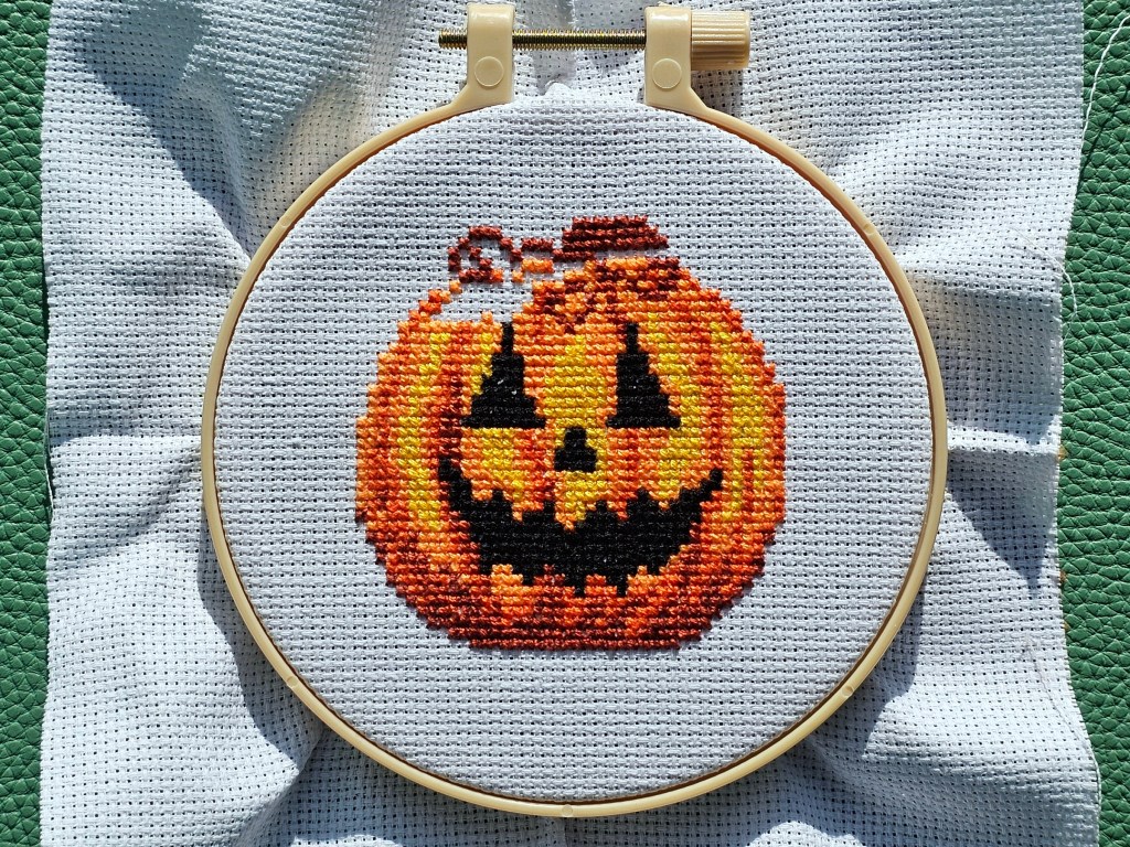 Nearly completed Jack-o'-lantern cross stitch design, with only the green leaf missing