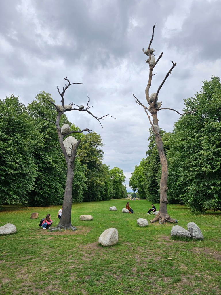 Realistic tree sculptures in Kensington Gardens. Two dry trees with no leaves have large rocks stuck between the branches.