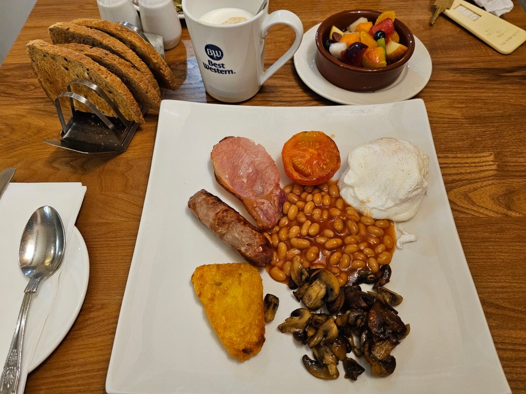 Full English breakfast consisting of baked beans, hash brown, mushrooms, tomatoes, bacon, sausage and poached eggs