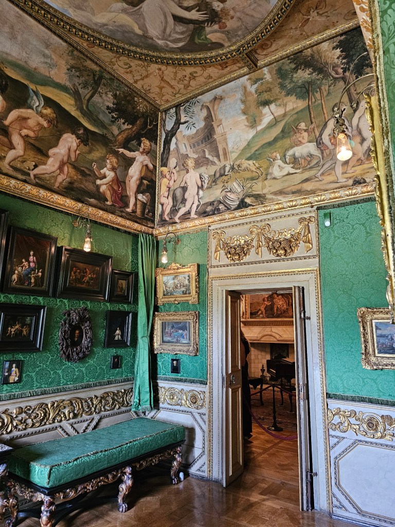 An elegant small room of Ham House, London. There is a green wallpaper on the wall, lots of small, framed paintings and gilded details.
