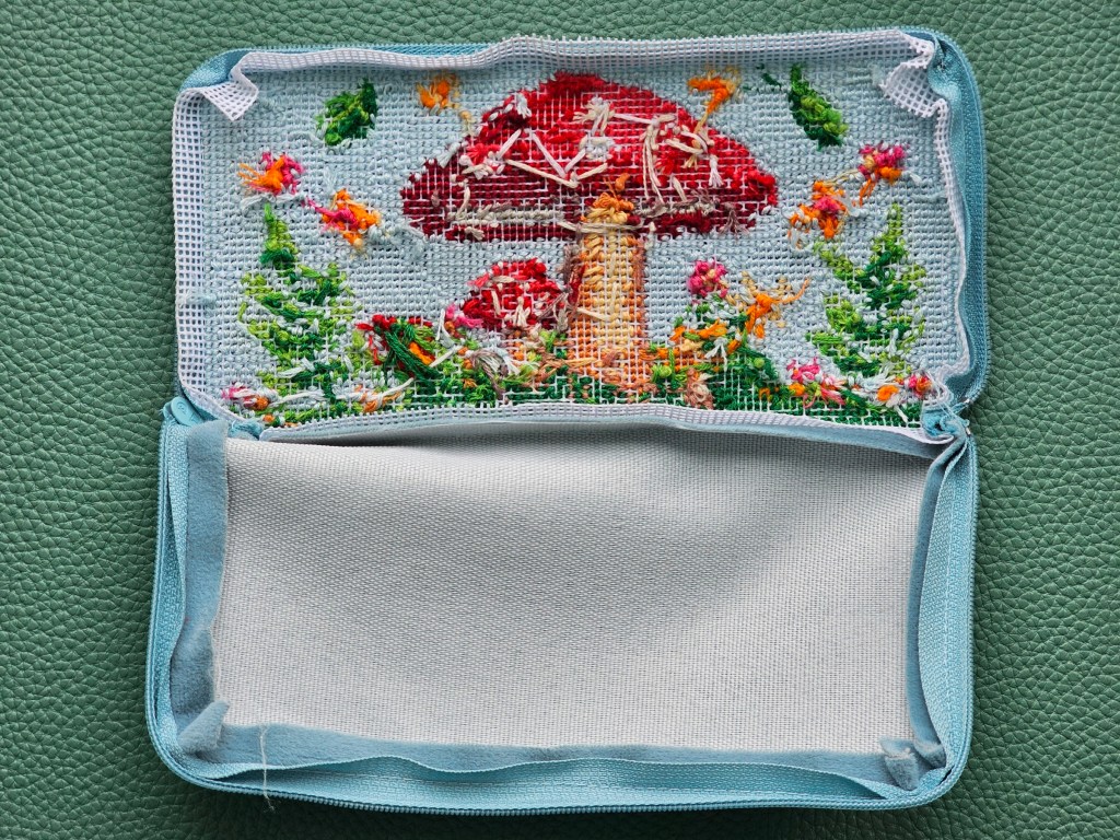 The wrong side of a finished DIY zip case with a half stitch design featuring colourful mushrooms