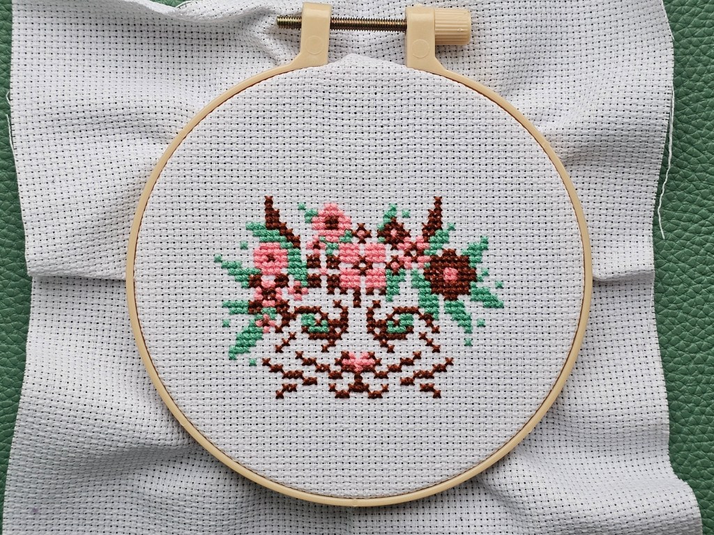 Partially finished mini cross stitch project featuring a floral cat.