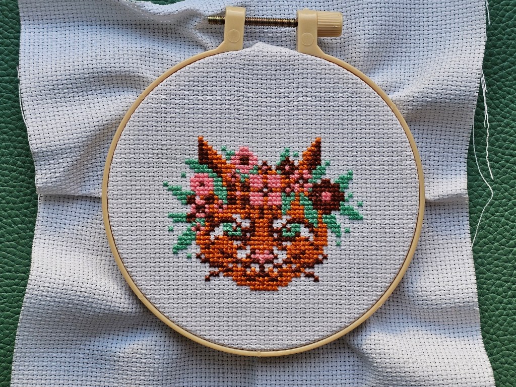 Partially finished mini cross stitch project featuring a floral cat.