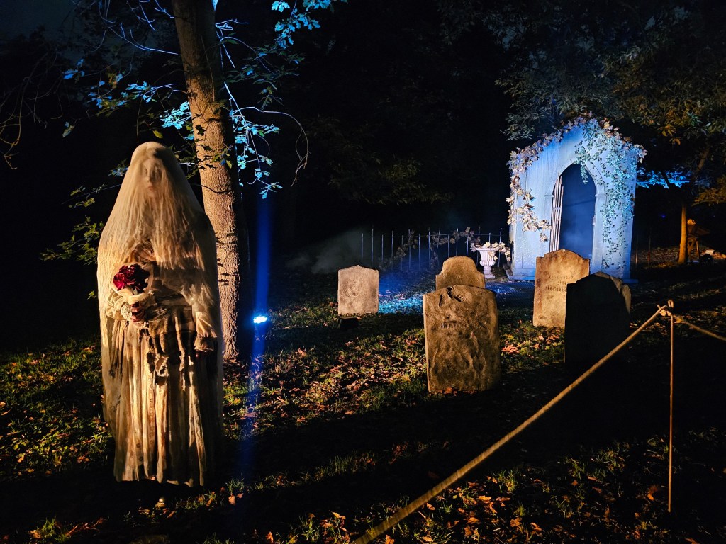 A person dressed up as Corpse Bride, standing next to faux tombstones in Kew Gardens, during a Halloween display