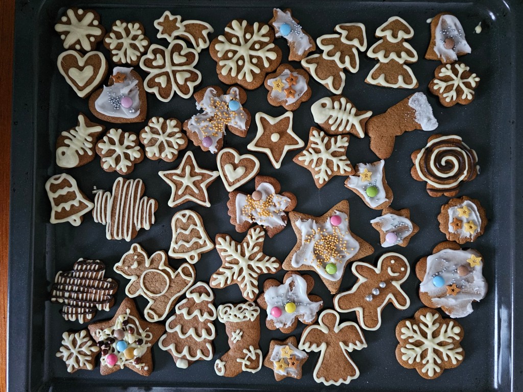 A baking sheet with cut-out, baked gingerbread cookies in various shapes, decorated with white chocolate and icing.
