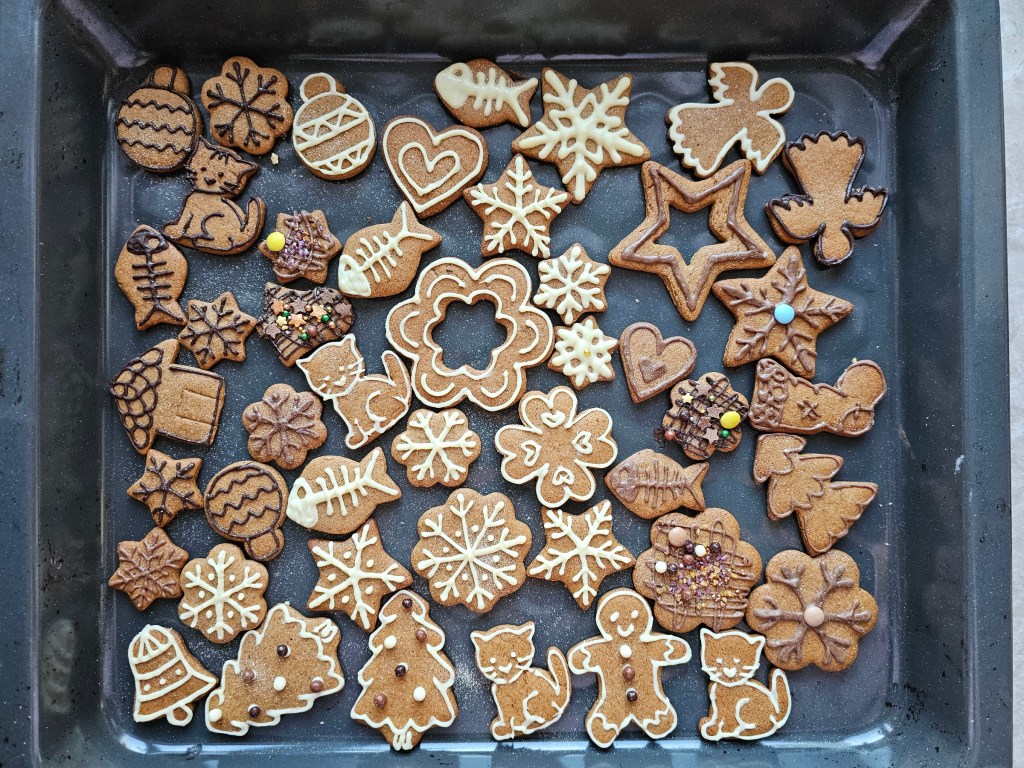 A baking sheet with cut-out, baked gingerbread cookies in various shapes, decorated with white and milk chocolate.