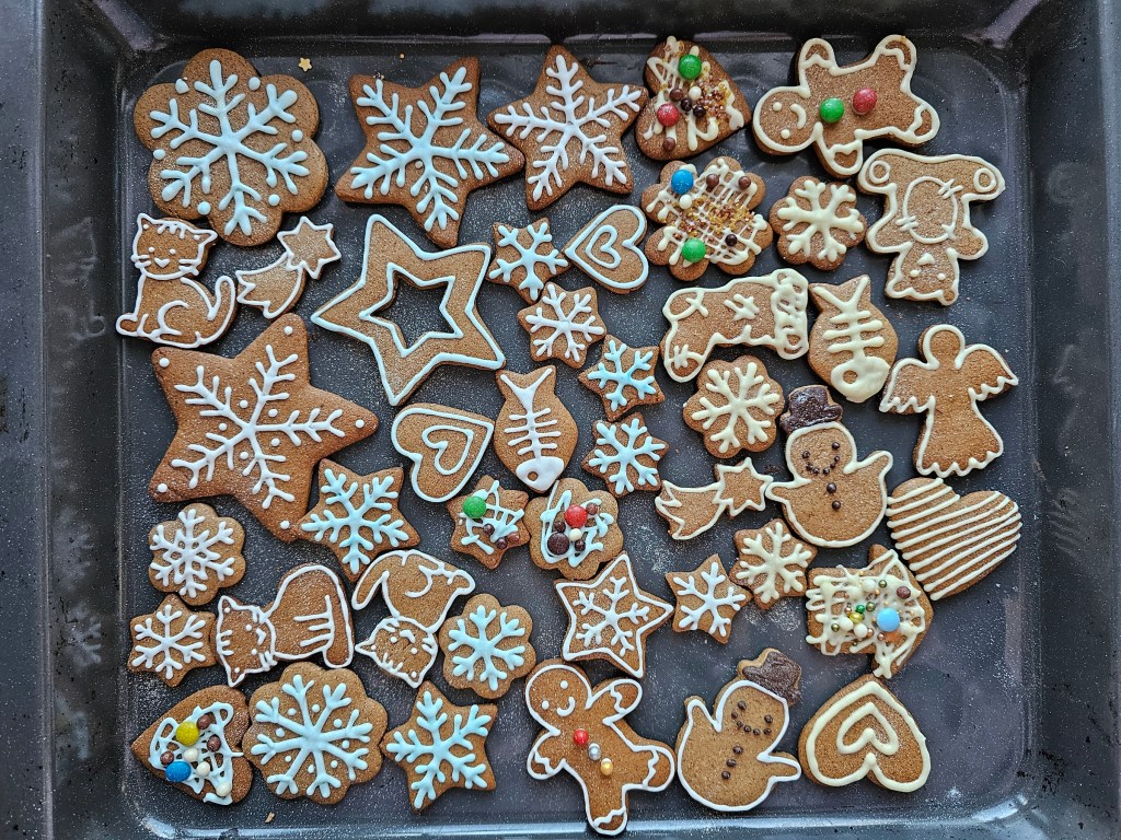 A baking sheet with cut-out, baked gingerbread cookies in various shapes, decorated with white chocolate and blue icing.