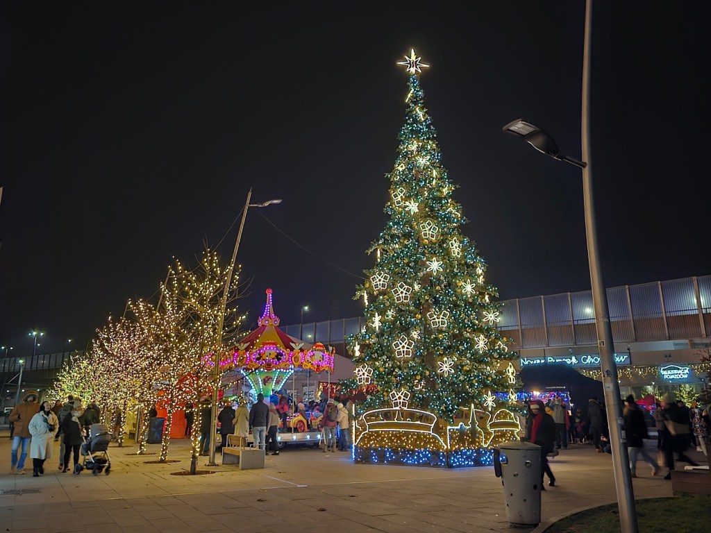 A Christmas tree and illuminated trees at a small Christmas market at night