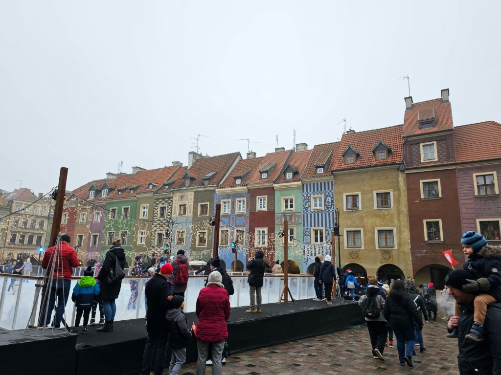 Poznan town square during the Christmas market on an overcast day. There's a small ice rink with people skating.