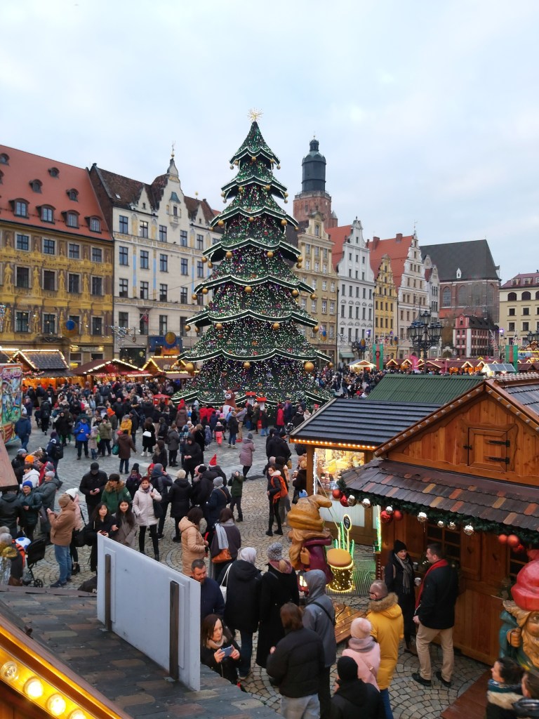 Wroclaw Christmas market by day. There are various stands, crowds of people and a huge Christmas tree
