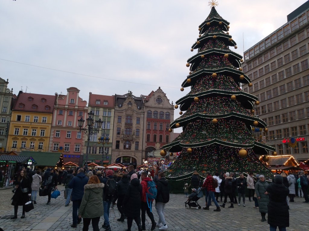 Wroclaw Christmas market by day. There are various stands, crowds of people and a huge Christmas tree