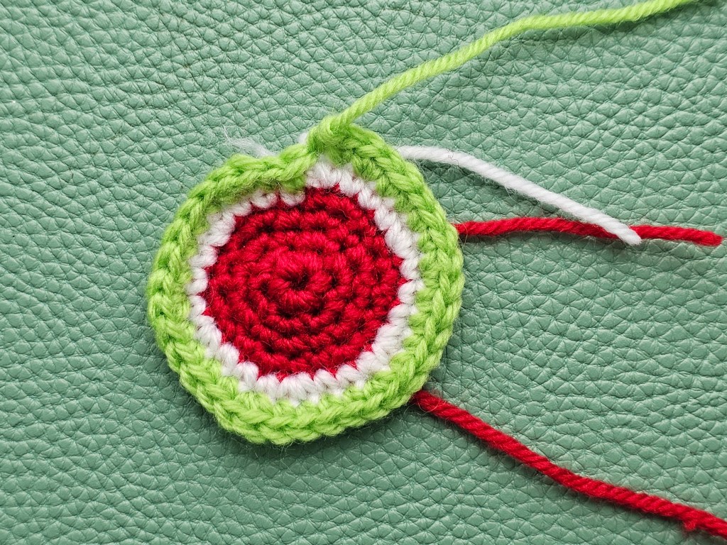 Making a crocheted watermelon keychain - nearly done - rounds of red, white and light green are crocheted.