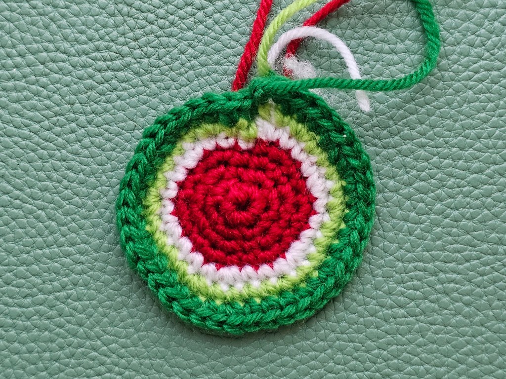 Making a crocheted watermelon keychain - nearly done - rounds of red, white and green are crocheted.
