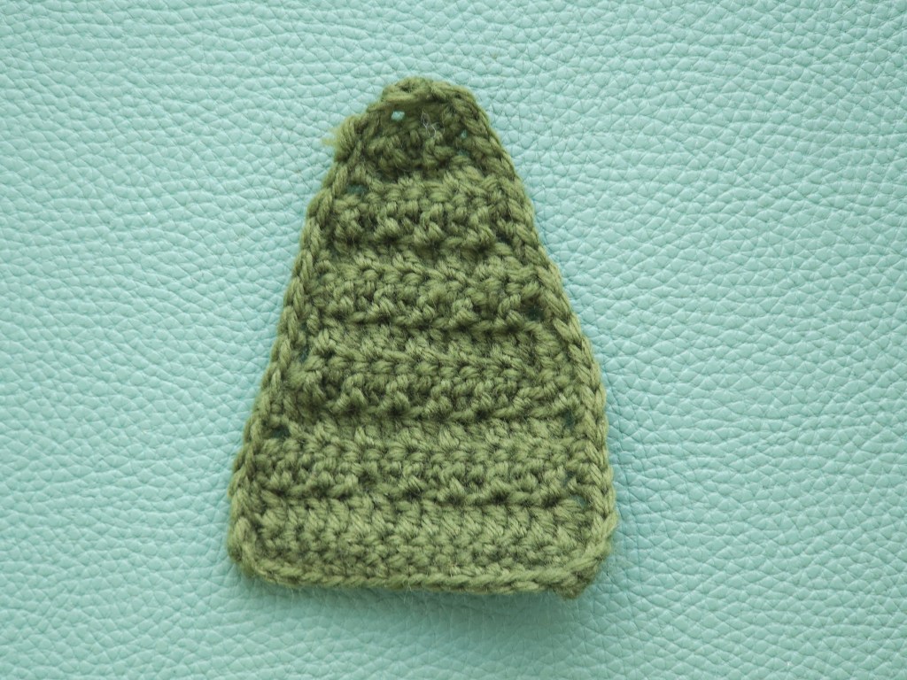 Crocheted green triangle with neat stitches on the edges, supposed to represent a Christmas tree.