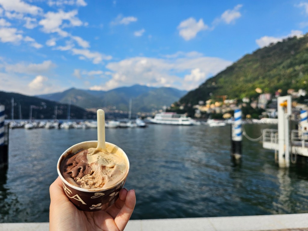 A person holding gelato in a cup, next to lake Como